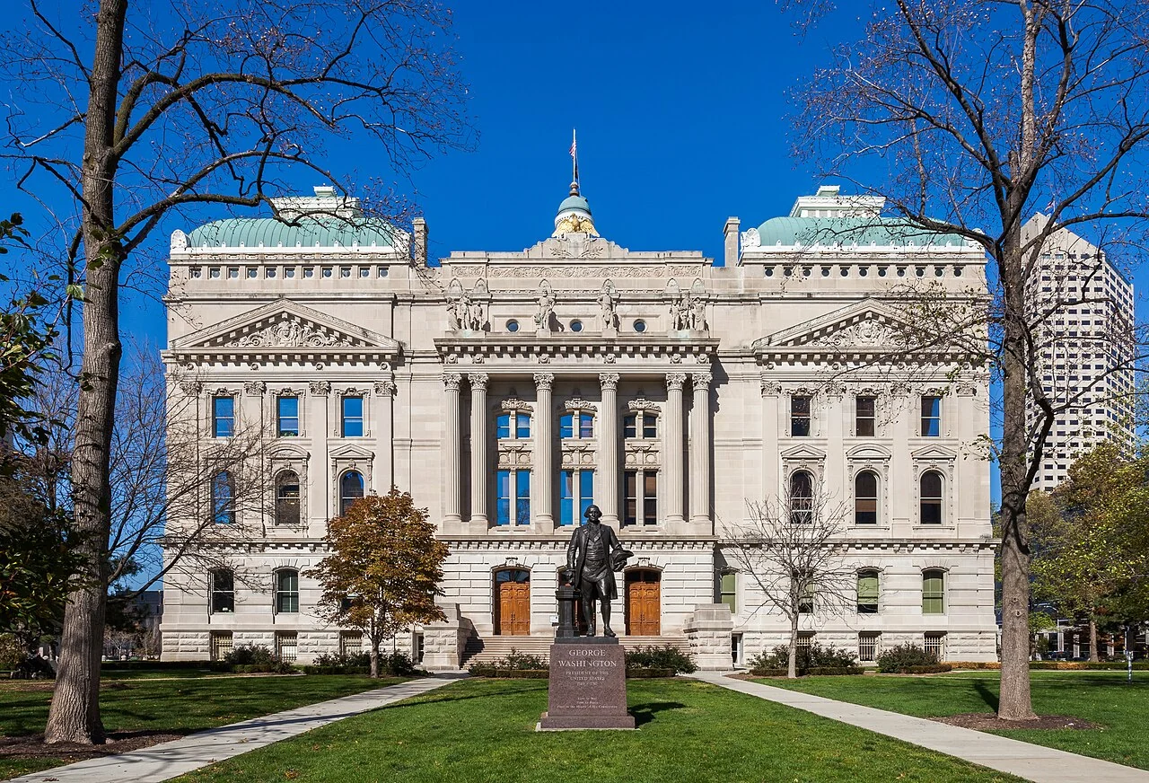 The south facade of the Indiana Statehouse with lawn and a statue in the foreground.