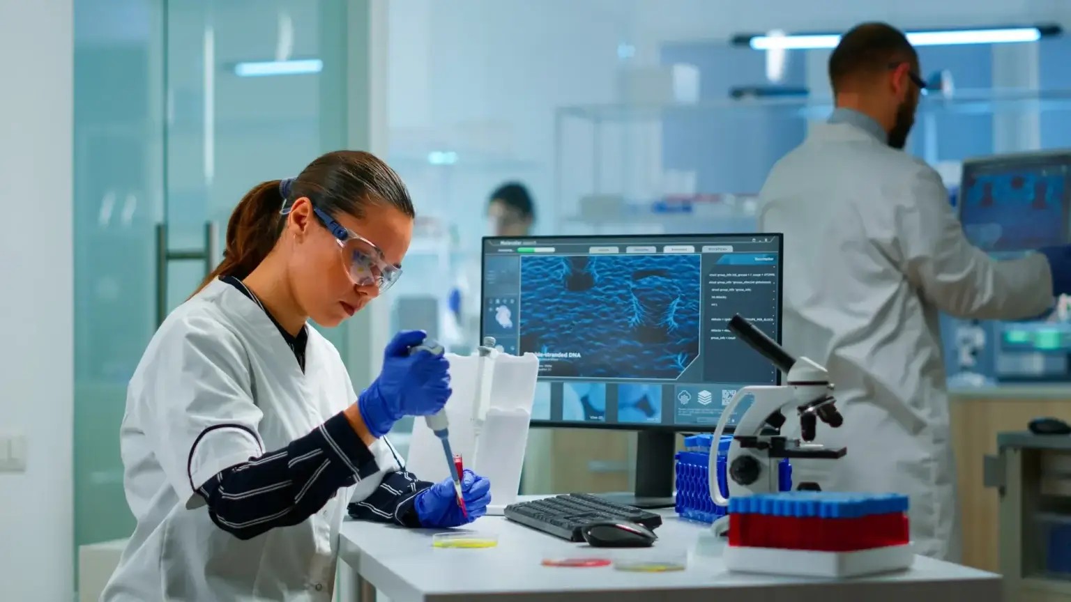 Laboratory scientist working with a pipette beside a microscope and computer